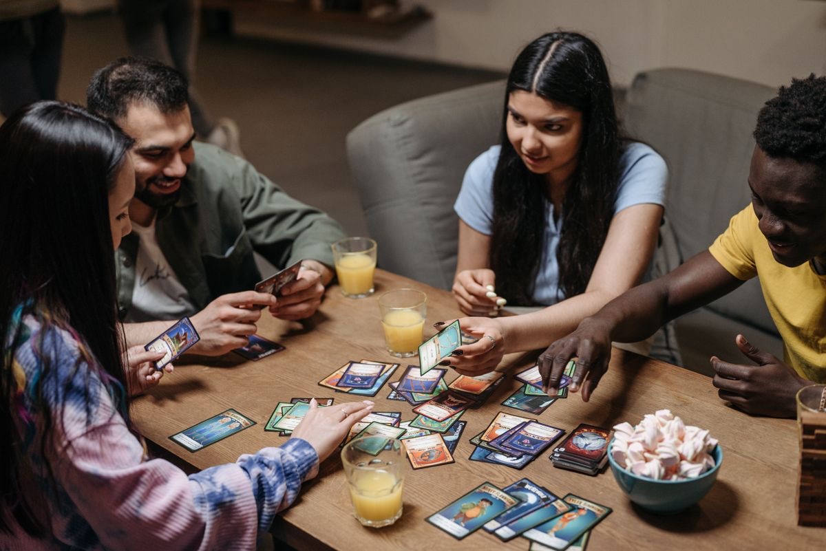 Four friends laughing over a card game spread across a table