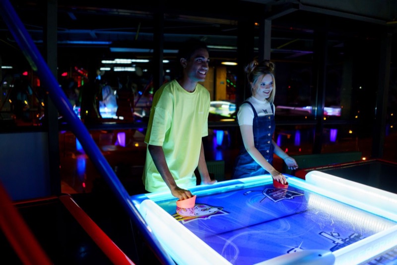 Two friends laughing over a game of air hockey at an arcade